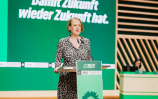 Lisa steht am Redepult und redet.